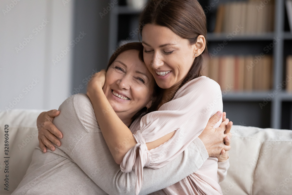 Head shot happy young woman hugging excited old senior mother, glad to hear good news. Smiling grownup daughter embracing pleasant kind middle aged mommy, resting on comfortable sofa at home. Head shot happy young woman hugging excited old senior mother, glad to hear good news. Smiling grownup daughter embracing pleasant kind middle aged mommy, resting on comfortable sofa at home.