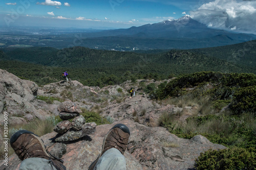 paisaje montañoso con un hombre sentado mostrado los pies junto a una pila de rocas. Hombre practicando campista en la montaña cargando su mochila.