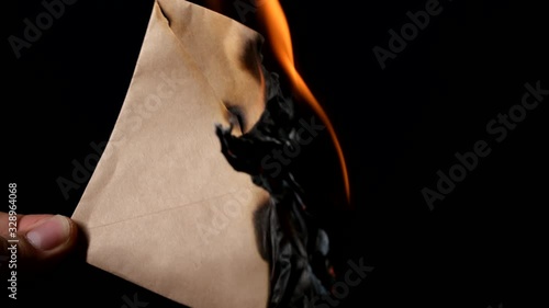 Close up view of male hand holding burning vintage letter envelope isolated on black.