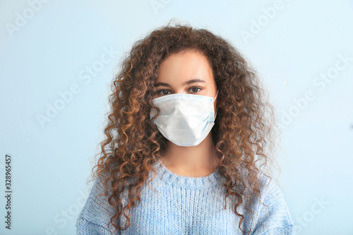 Young woman with protective mask on light background. Concept of epidemic photo