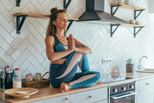 Fit concentrated caucasian woman sitting on talbe in kitchen and meditating photo