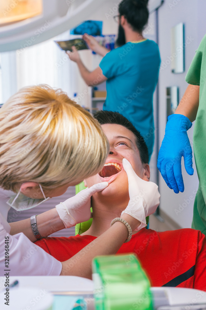 Female dentist with the help of her dentist technician examines the mouth and teeth of a teenage boy patient. Female dentist with the help of her dentist technician examines the mouth and teeth of a teenage boy patient.