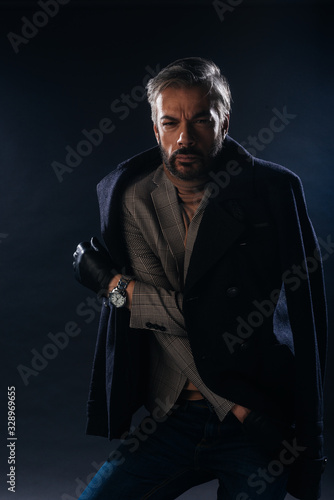 Portrait of a formal dressed handsome adult man with grey hair posing inside a studio on a black background..