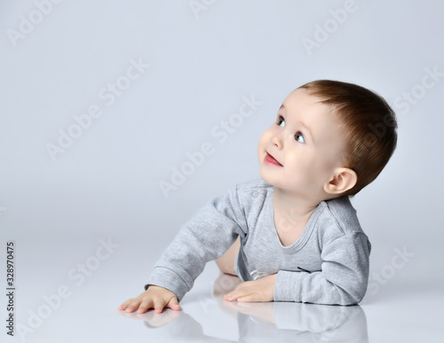 Little baby boy toddler in grey casual jumpsuit and barefoot lying on floor, smiling and looking up photo