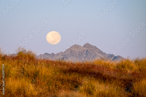 orane moon above the mountains. yellow grass on the foreground photo