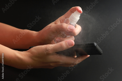Woman hands using hand sanitiser spray on smartphone, protection from coronavirus. Hygiene and Healthcare concept.
