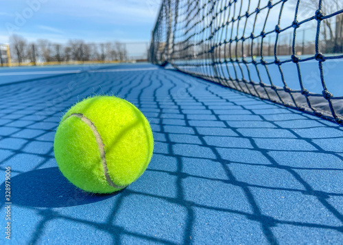 Tennis ball on a soft blue court next to the net. outside tennis court © EvgeniiAnd
