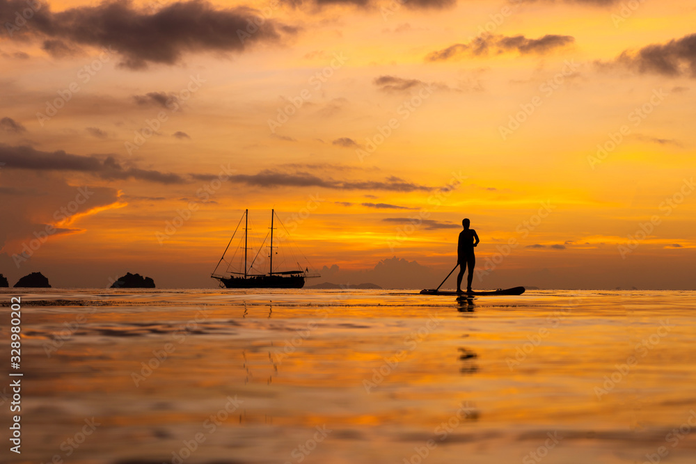 Colorful sunset on a tropical beach. Orange sunset on the ocean. Colorful sunset in the tropics. A pair of people are swimming on sup boards