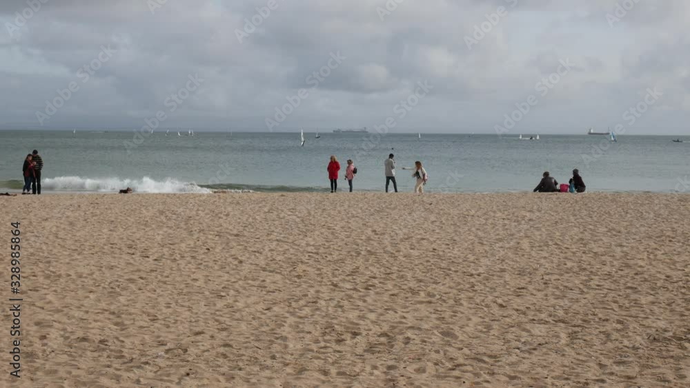A few people relaxing on a beach during a cold windy cloudy day A few people relaxing on a beach during a cold windy cloudy day