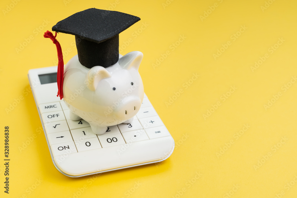 Student loan payment calculation, scholarship or saving for school and education concept, white piggy bank wearing graduation hat on calculator on yellow background with copy space - obrazy, fototapety, plakaty 