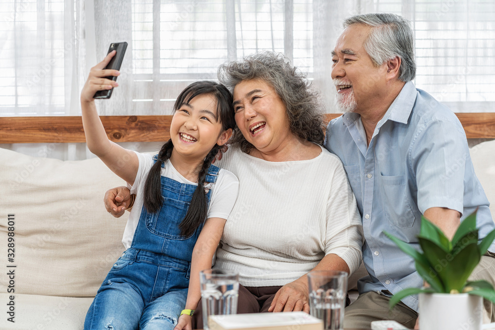 Asian Granddaughter taking selfie with couple Grandparent with happy feeling by mobile phone in house, Long live and Elderly society, Warm family and happiness, leisure and lifestyle concept