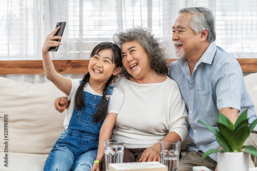 Obraz na płótnie Asian Granddaughter taking selfie with couple Grandparent with happy feeling by mobile phone in house, Long live and Elderly society, Warm family and happiness, leisure and lifestyle concept w salonie