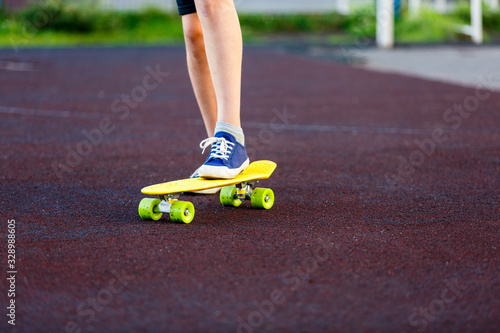 Close up legs in blue sneakers riding on yellow skateboard in motion. Active urban lifestyle of youth, training, hobby, activity concept. Active outdoor sport for kids. Child skateboarding.