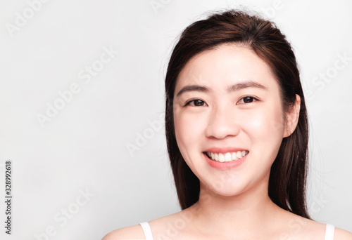 young beautiful asian woman with clean and bright skin, Cosmetic Beauty Concept,hands touch on the cheek, smiling and friendly face isolated on grey background