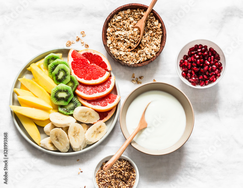 Breakfast set table - fresh tropical fruits, greek yogurt, granola on a light background, top view. Delicious healthy diet food concept. Flat lay