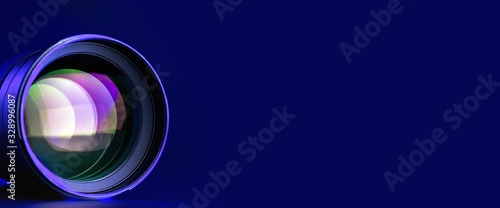 Banner. The camera lens with multi-colored illumination on a blue background.  Right place for text. Optics. .