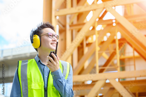 Young asian engineers are working on the construction site. Wear a yellow earmuff sound protection and uniform staff. Hand holding portable radio transceiver for communication