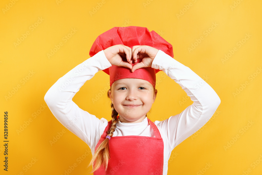 Happy beautiful little girl chef on a yellow background. The child shows the heart with his fingers Happy beautiful little girl chef on a yellow background. The child shows the heart with his fingers