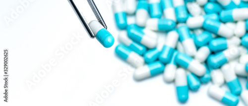 Forceps pick white-blue capsule from group of capsule pills. Drugs choose. Antibiotic drug selection. Antibiotic drug resistance concept. QA and QC in pharmaceutical factory concept. Drugs of choice.