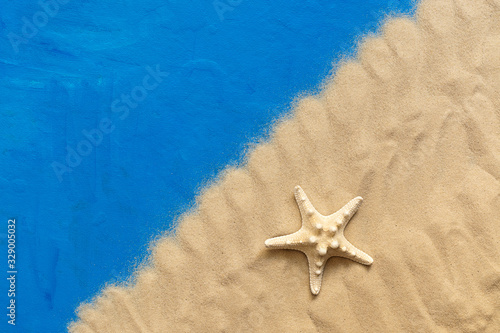 Creative composition of sea sand and starfish on a blue painted background. The concept of summer vacation and relaxation. Top view, flat lay, corner frame.