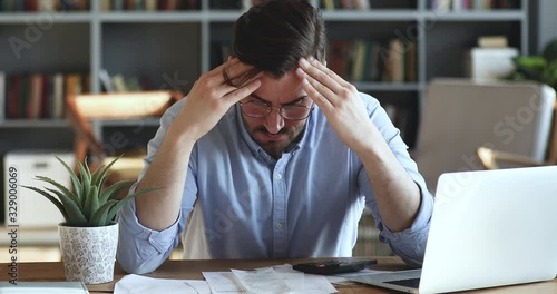 Depressed desperate man feeling worried about financial problem doing paperwork. Stressed businessman looking frustrated thinking of money debt, budget loss, bankruptcy sitting at home office desk.