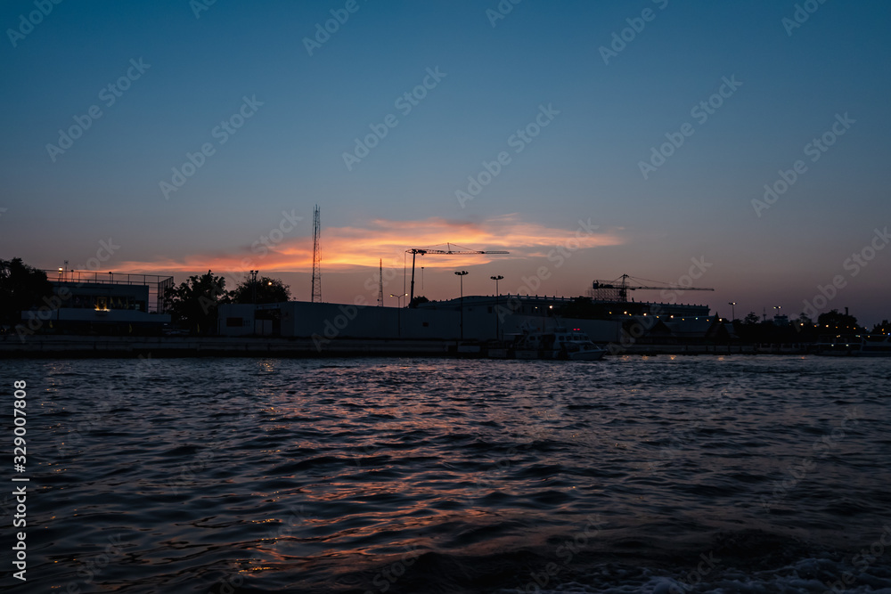 Sunrise or sunset view of Chao Phraya River , Bangkok, Thailand . Shows water transport. reflective of the sun. Image contain certain grain or noise and soft focus