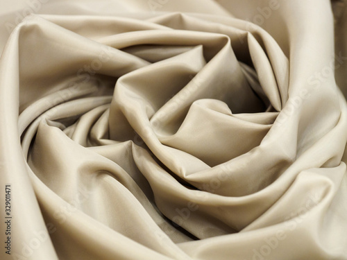 Beige shiny fabric lying in folds in the shape of a rose flower for sale in a store. The concept of fashionable clothes and interior