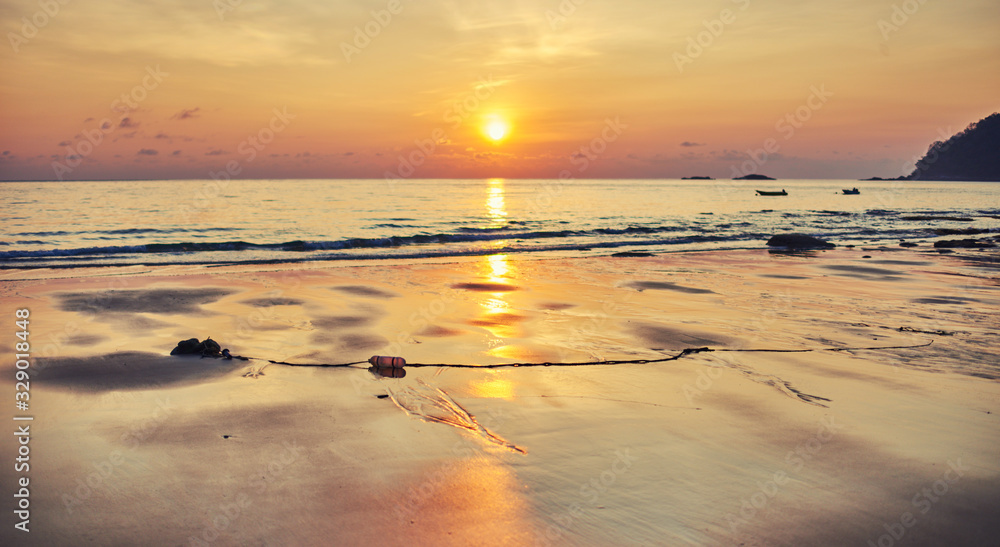 Amazing beach sunset with endless horizon and lonely boat in the distance, and incredible orange sun. Golden sunrise or sunset over the sea or ocean.