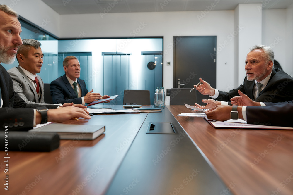 Multicultural business people in formal wear discussing something while having a meeting with partners in the modern office Multicultural business people in formal wear discussing something while having a meeting with partners in the modern office