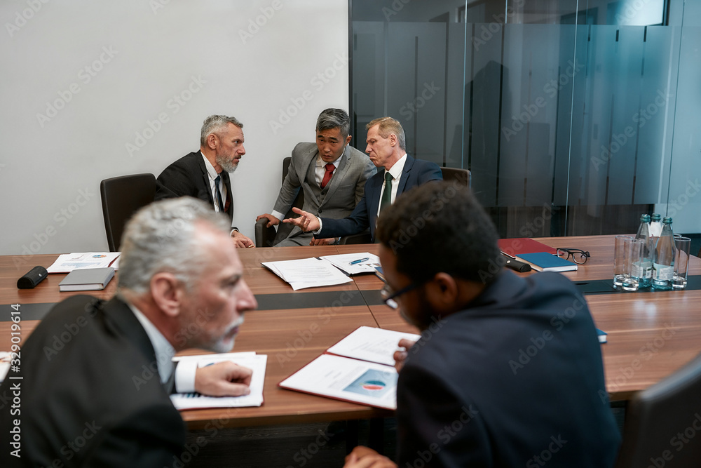 Multicultural business people in formal wear discussing contract conditions while having a meeting with partners in the modern office Multicultural business people in formal wear discussing contract conditions while having a meeting with partners in the modern office