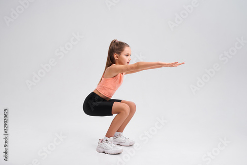 Commit to be fit. Flexible cute little girl child looking aside while doing sit ups isolated on a white background. Sport, training, fitness, active lifestyle concept. Horizontal shot