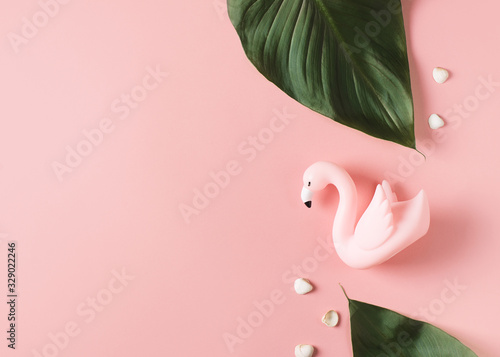 Creative pastel falt lay with tropical leaves and mini flamingo on pink background photo