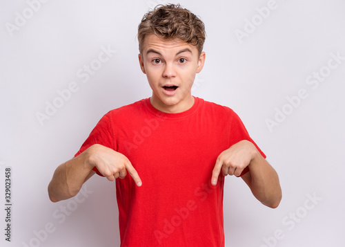 Portrait of handsome teen boy pointing oneself, on grey background. Emotions and signs concept. Happy smiling child looking at camera. Young student points fingers at himself
