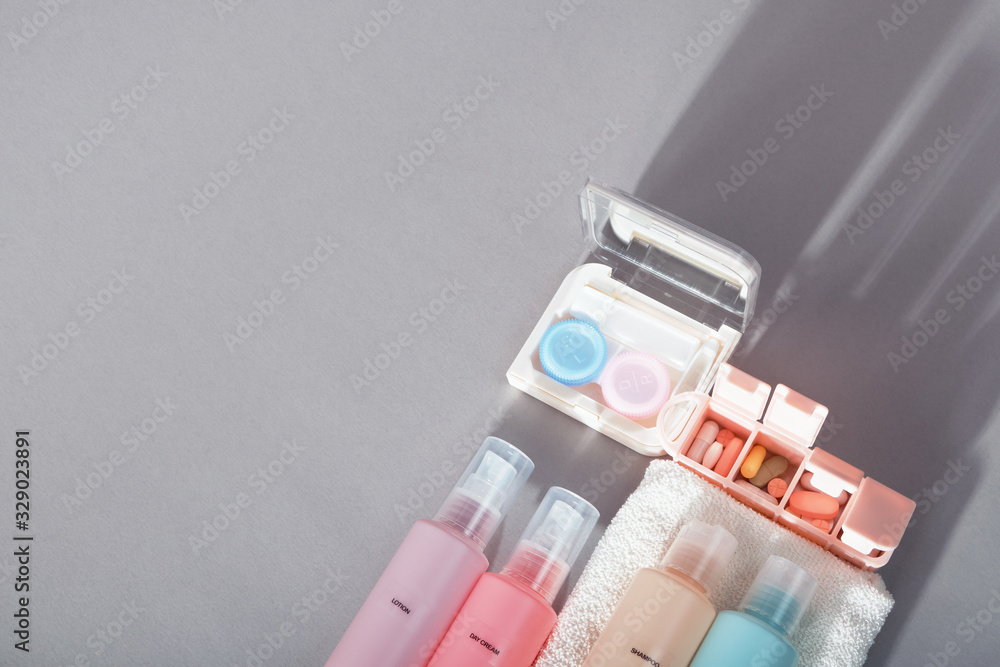 Travel kit. Set of four small plastic bottles for cosmetic products, kit for contact lenses, pill organizer, towel. Gray background with shadows. Travel kit. Set of four small plastic bottles for cosmetic products, kit for contact lenses, pill organizer, towel. Gray background with shadows.