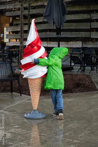 A small boy in a bright green raincoat hugs a mockup of a large ice cream on a street wet with rain