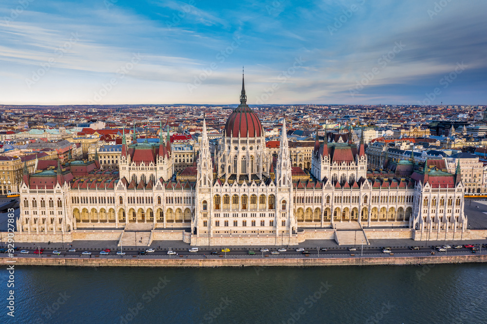 Budapest, Hungary - Aerial drone view of the beautiful Hungarian Parliament building with warm colors at sunset. Afternoon traffic, River Danube, traditional yellow trams and blue sky at background
