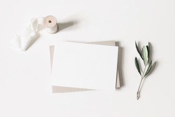Summer wedding stationery mock-up scene. Blank horizontal greeting card, envelope, ribbon and olive branches isolated on white table background. Feminine Mediterranean flat lay, top view.