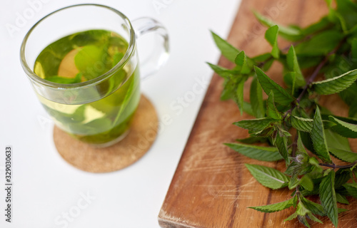 drinks, herbs and ethnoscience concept - herbal tea with fresh peppermint on wooden board