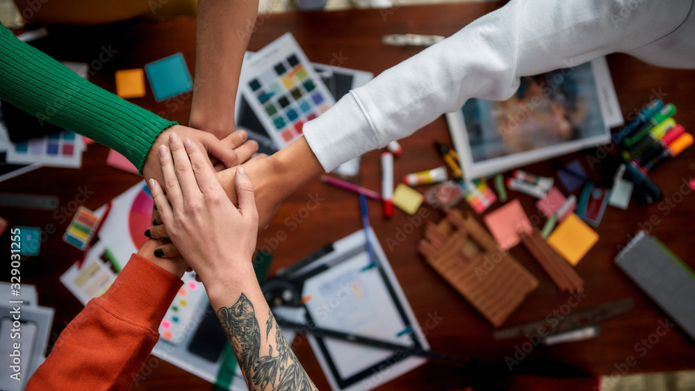 Great job. Group of multicultural creative people stacking hands over the desk with graphic designer's work tools and equipment on it. Web design concept. Teamwork
