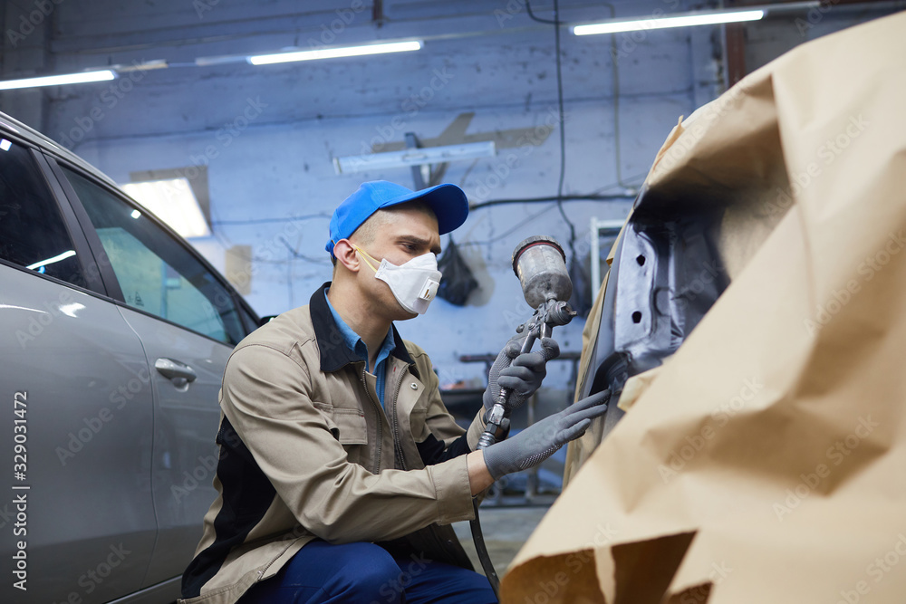 Horizontal medium shot of professional car painter in protective workwear working in auto service center, copy space