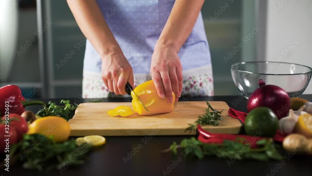 Woman Hands Slicing Yellow Bell Pepper on the Wooden Cutting Board with Knife in the Kitchen. Slow Motion. Natural Organic and Vegan Healthy Food Concept Woman Hands Slicing Yellow Bell Pepper on the Wooden Cutting Board with Knife in the Kitchen. Slow Motion. Natural Organic and Vegan Healthy Food Concept