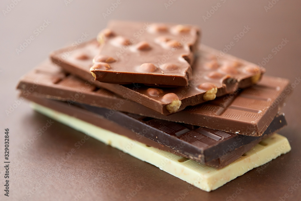 sweets, confectionery and food concept - bars of dark, white and milk chocolate with nuts on brown background