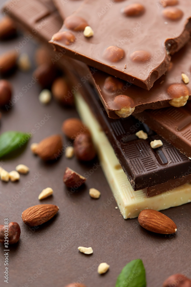 sweets, confectionery and food concept - bars of dark, white and milk chocolate with nuts on brown background