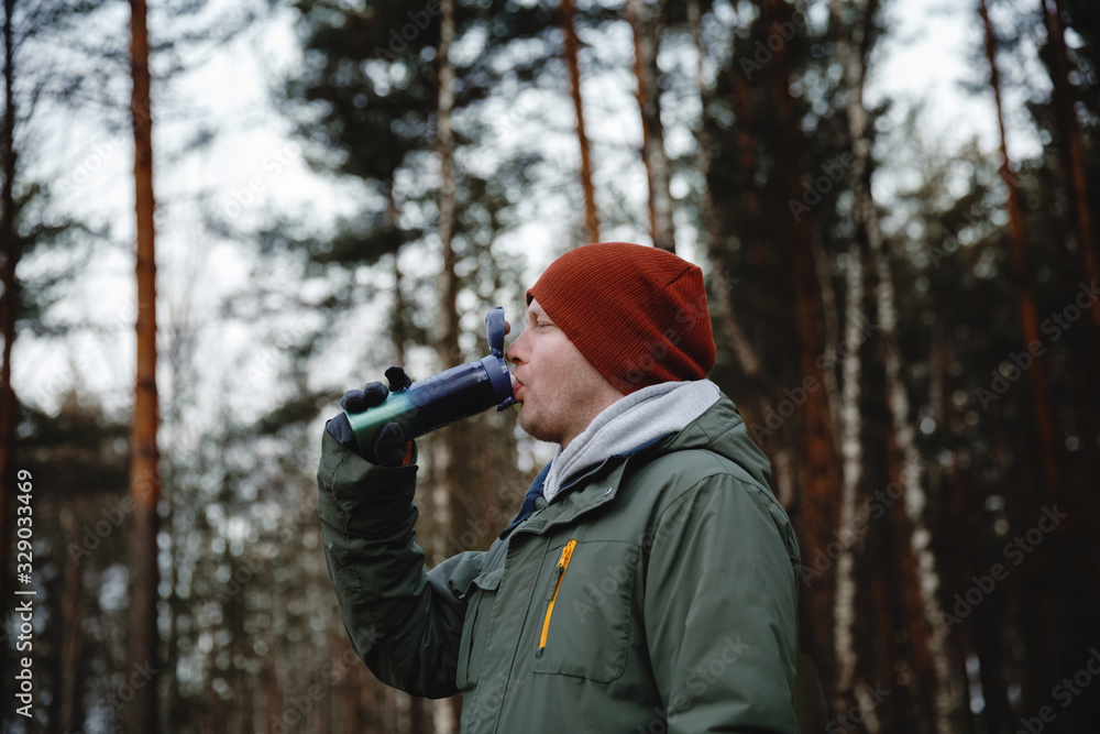 a Man drinks from thermos in nature.