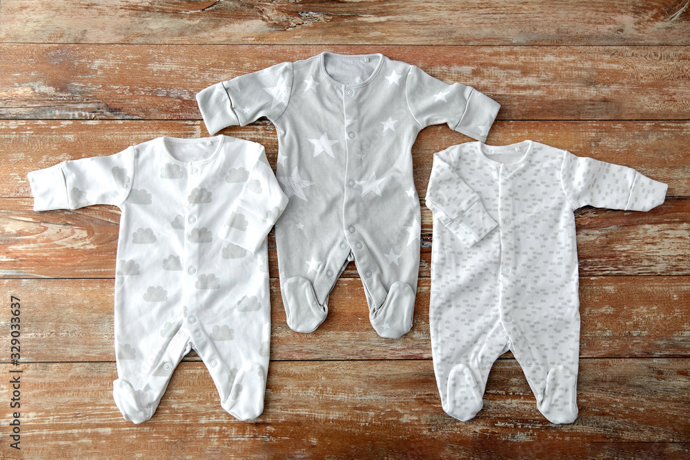 Φωτογραφία babyhood and clothing concept - baby clothes set of bodysuits and socks on woode