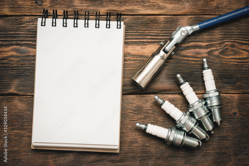 Spark plugs and blank page notepad with copy space on brown wooden workbench background. - obrazy, fototapety, plakaty 