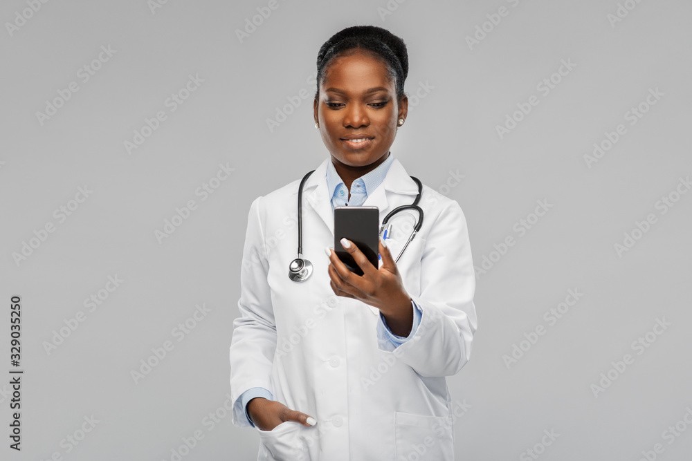 medicine, technology and healthcare concept - happy smiling african american female doctor or in white coat with smartphone and stethoscope over background medicine, technology and healthcare concept - happy smiling african american female doctor or in white coat with smartphone and stethoscope over background