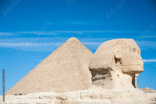 Bright sunny view of the crumbling profile of the Great Sphinx of Giza standing in front of the Great Pyramid on the Giza plateau  Egypt