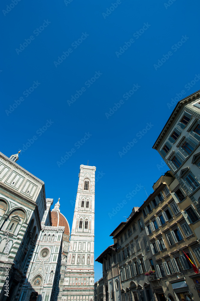 Dramatic blue sky view of the Piazza del Duomo with Giotto's Bell Tower standing above the dome of the cathedral in Florence, Italy
