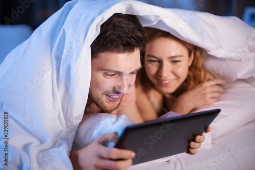 technology, internet and people concept - happy couple using tablet pc computer in bed at night